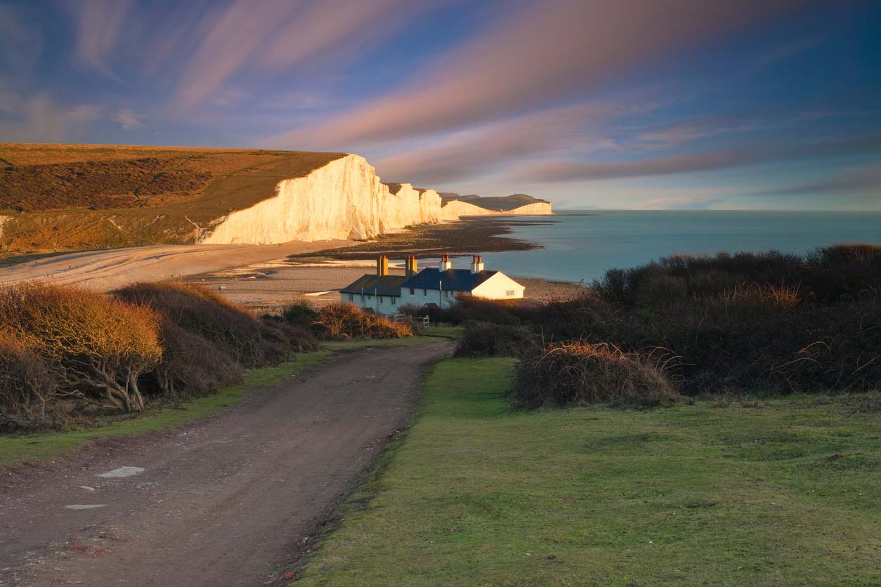 Sunset over the famous coastal cottages at Seven Sisters, East Sussex, UK. White chalk cliffs shimmer in the light of sunset.
