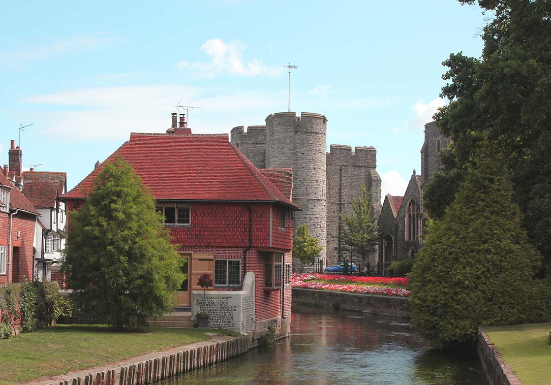 The River Stour passing through the city centre of Canterbury with houses and the Westgate tower.