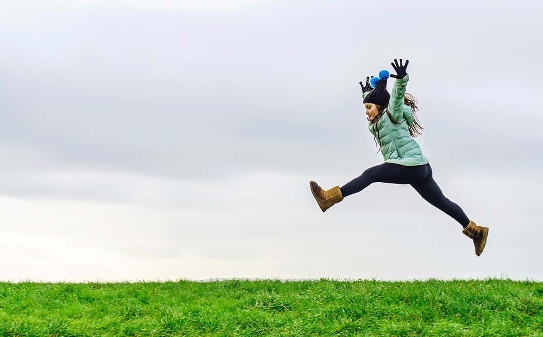 Girl leaping into the air, on a grassy field.