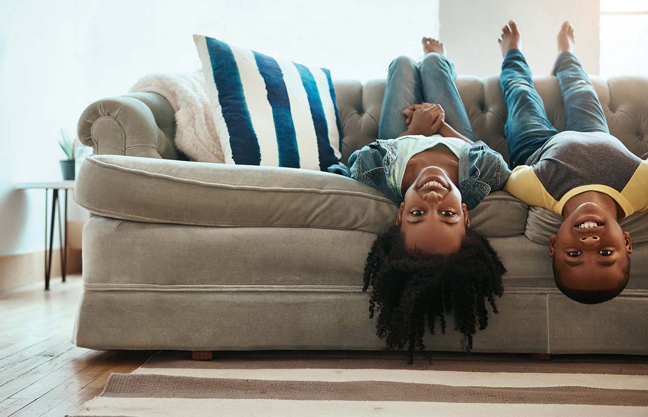 Image of two smiling American children lying upside down on a sofa.
