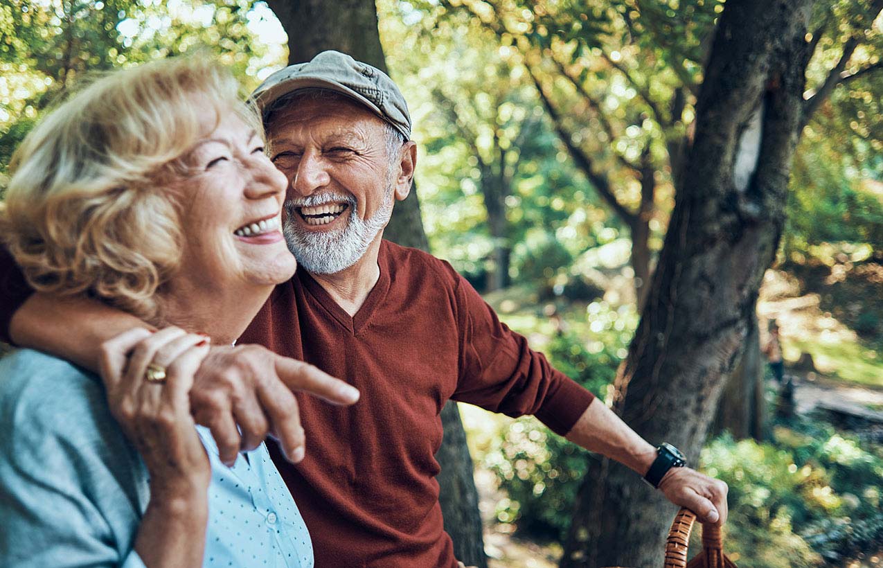 Elderly couple enjoying their time together and laughing on a bench in the forest.
