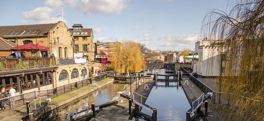 A canal barge travelling down Camden Lock canal, with buildings in the background.